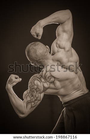 Muscle man with tattoos on dark background.Sepia