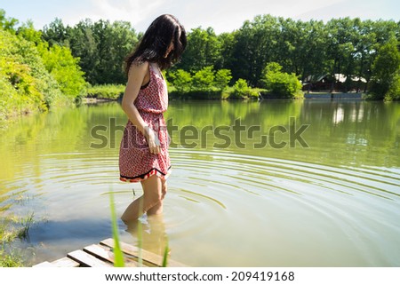 Brunette stands knee-deep in water in the middle of the lake. Girl enjoying the cool water on a hot summer day. Girl, lake, cool, sun - concept holiday. The idea of ??an article on summer vacation.