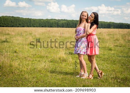 Two young girls standing in a wheat field. Beautiful girlfriends to enjoy all the sun and nature. Sky, field, sun, wheat, friends - Concept of relaxing and friendly. Article about nature, friendship.
