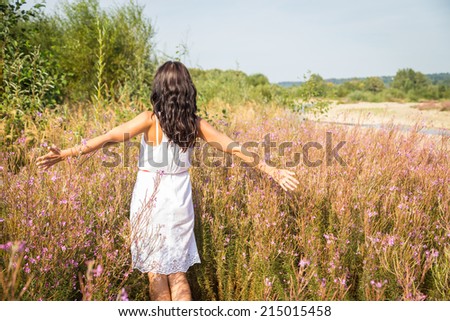 Young brunette woman in a white dress. A girl stands in the middle of pink flowers field on a sunny day. Field, flowers beauty, nature - The concept of country vacation. Article about vacation.