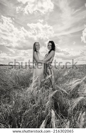 Two young girls standing in a wheat field. Beautiful girlfriends to enjoy all the sun and nature. Sky, field, sun, wheat, friends - Concept of relaxing and friendly. Article about nature, friendship.
