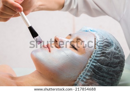 Spa therapy for young woman receiving facial mask at beauty salon - indoors.Beautiful woman with facial mask at beauty salon.Woman with clay facial mask in beauty spa