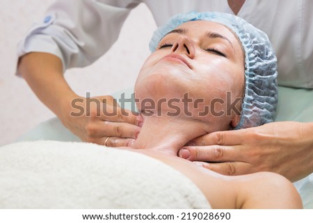 Young woman in a spa lying with her eyes closed. The therapist gives her a facial massage. Beautician applying cosmetic cream. Cosmetology, facial, beauty - The concept of facial skin care.