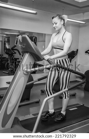 The beautiful blonde on a treadmill. Black and white photography.Cute young woman exercising on a treadmill at a gym.Attractive young fitness model runs on a treadmill,is engaged in fitness sport club
