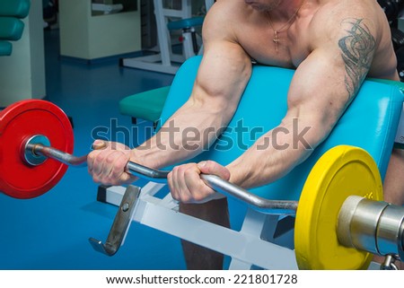 Closeup of a muscular young man lifting weights in the gym.Man makes exercises. Sport, power, dumbbells, tension, exercise - the concept of a healthy lifestyle. Article about fitness and sports.