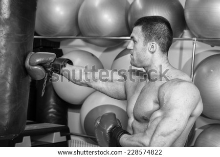 Muscular man in the gym. The man in boxing gloves, hit a punching bag, exercise. Boxing, workout, muscle, strength, power - the concept of strength training and boxing