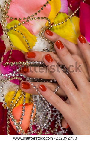Beautiful hands with a nice manicure. Gel nails are covered with red polish. Spa treatment for hands. Spa treatment, bath for hands. Hands on a background of rose petals in spa salon.