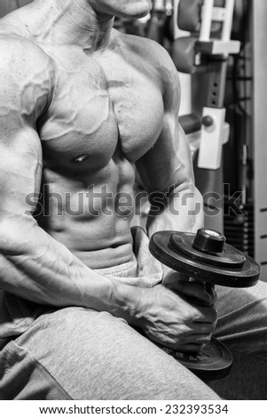 Handsome muscular man working out with dumbbells in gym.Sport, power, dumbbells, tension, exercise - the concept of a healthy lifestyle. Article about fitness and sports.