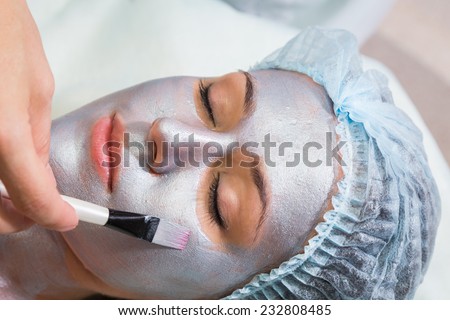 Young woman at spa procedures applying mask. Therapist applying a face mask to the face of a beautiful young  woman using a cosmetic brush.Cosmetology,facial, beauty - The concept of facial skin care.