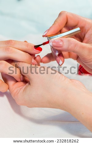 Manicure. applying red nail polish. Closeup of Woman applying nail varnish to finger nails.Manicure process.Beautiful manicure process. Nail polish being applied to hand, polish in red color