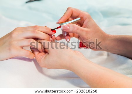 Manicure. applying red nail polish. Closeup of Woman applying nail varnish to finger nails.Manicure process.Beautiful manicure process. Nail polish being applied to hand, polish in red color