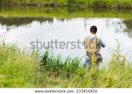 Fisherman on the river bank. Man fisherman catches a fish. Fisherman in his hand holding spinning. Fishing, spinning reel, fish, Breg rivers. - The concept of a rural getaway. Article about fishing.