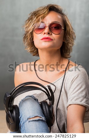 Blonde in headphones. Stylish girl in casual clothes on a gray background. Blonde posing in the studio.