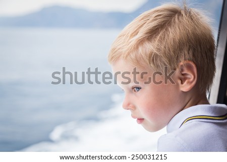The boy looks at the sea from the deck of the ship. Boy with blond hair in a good mood on the deck, watching the sea.Sea voyage.