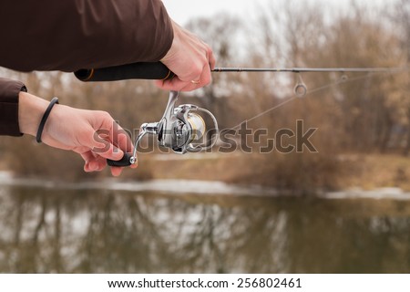 Winter spinning. Fishing in winter. Fisherman on the river bank. Fisherman holding a light spinning rod in his hand. Suburban recreation, sport fishing. Active Life on a fishing trip.