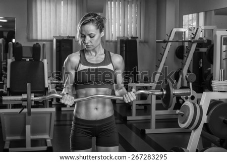 Female fitness. Blonde with a perfect figure, training in the gym. Athletic girl delat exercises with barbell. Strength training.