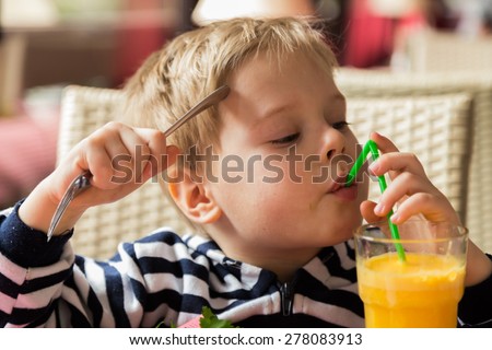 The boy has breakfast. Kid drinking orange juice. Breakfast. Little boy eating breakfast and greens.