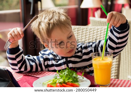 The boy has breakfast. Kid drinking orange juice. Breakfast. Little boy eating breakfast and greens.