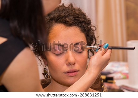 Work of make-up artist. Makeup artist apply makeup on the face of the girl model. Painting of eyebrows. Application of shadows on the model\'s eyes.
