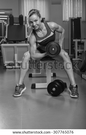 The sports girl with weights in the gym. Work on the body. Training and training of professional bodybuilder. Beautiful blonde with sports equipment.