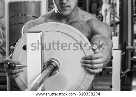 The athlete preparing for the bench press bar. Sports man in the gym. Attaching metal rings on the neck rod. Weight training. Work on muscles.