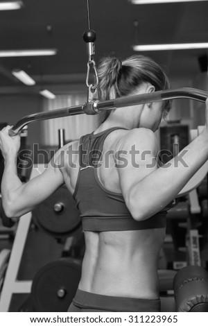 Young athlete working on your back muscles. Bench scales neck. Work on tell muscles. Beautiful blonde in the gym. Weight training.