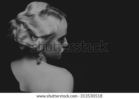 The blonde in a black dress on a dark background. Model in a beautiful black dress. Beautiful blonde on a dark background. Black and white photo. Jewelry\'s extraordinary. Design stylish way to model.