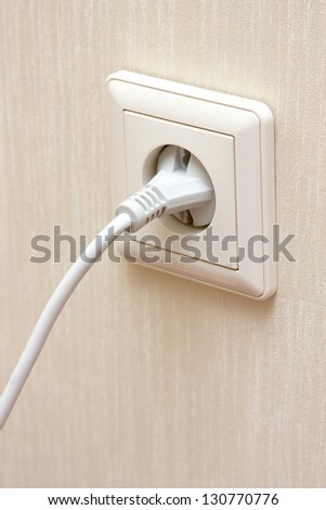 white electrical plug in the electric socket on a wall