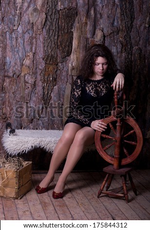 sad young woman with a spinning wheel in a rural black lace short dress