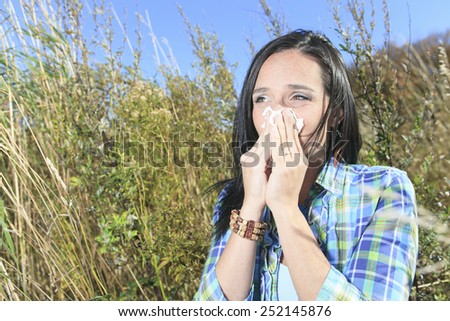 A Young woman sneezing in a field. Concept: seasonal allergy.