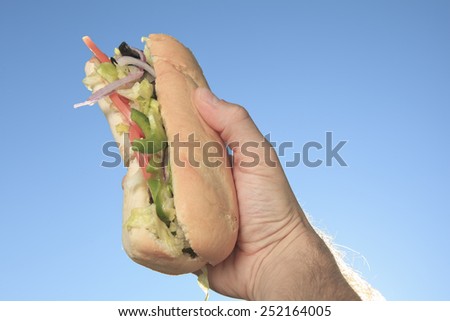 Hand holding sandwich with ham and tomato slices.