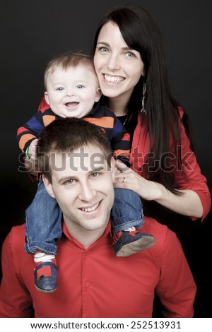 Happy family, father, mother and infant in front of a black background