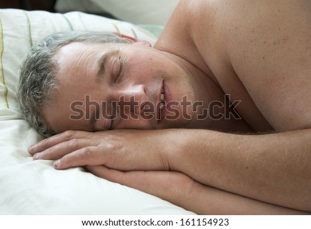 A mature white man asleep in bed with his head on his hands