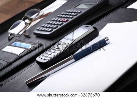 Black business briefcase open wide, with various office, computing and communication stuff inside, diagonal composition, skewed view