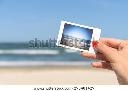 Girl Hand Holding Instant Photo Of Sea Beach Landscape, focus on hand