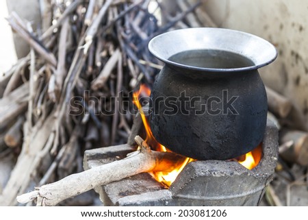 black pot boiling water for cooking on the fired stove next to firewood pile, Thailand Esan traditional culture ancient method