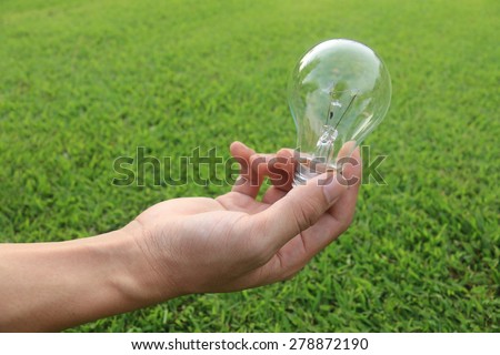 Energy saving concept. Hand holding light bulb on green grass background,.