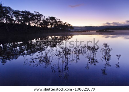 Jindabyne lake in snowy mountains, Australia, at Sunrise, pink and blue landscape with still water, mist and reflections