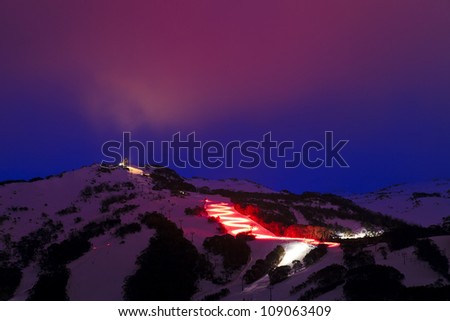 Night lightning skiing with red torch at Thredbo ski resort winter time at dusk with illuminated pink cloud