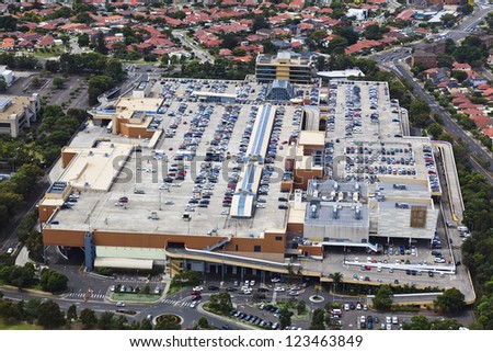 Birds view on shopping mall building with lots of parking, cars, people surrounded by village suburb of private houses