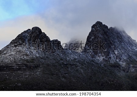 australia tasmania cradle mountain peaks rocks covered in snow behind wind and clouds at sunrise