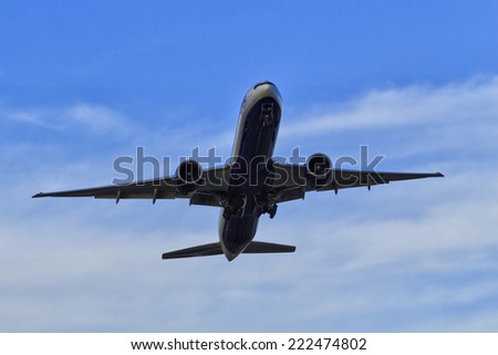 Commercial passenger airplane jet departing from airport rising altitude in blue sky with white clouds view from underneath
