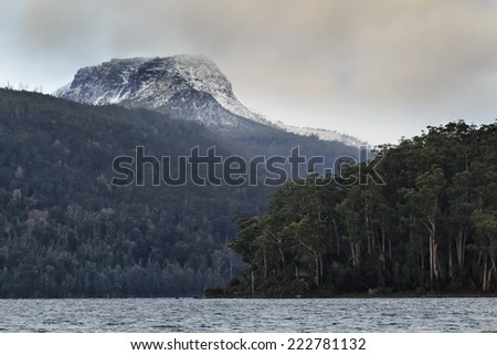 Australia Tasmania St Clair lake at sunrise remote snow covered mountain peak under winter clouds with lake shores covered in gum-tree woods