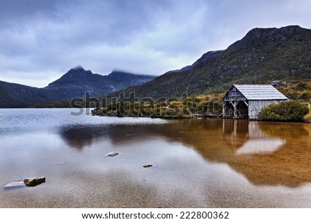 Australia Tasmania cradle mount and dove lake at sunset with heavy clouds hiding peak and still transparent clear water reflecting boatshed