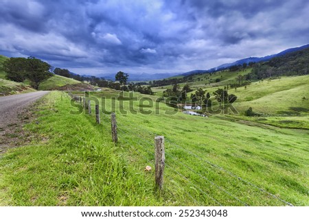 australian rural NSW remote agricultural farm with highly developed grazing land for steer production at cloudy thunderstorm weather view from side road over fence