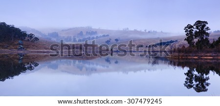 wide panoramic view around lake Lyell in Blue Mountains, Australia. Hills and woods of farm estate reflecting in still mist waters of mountain lake