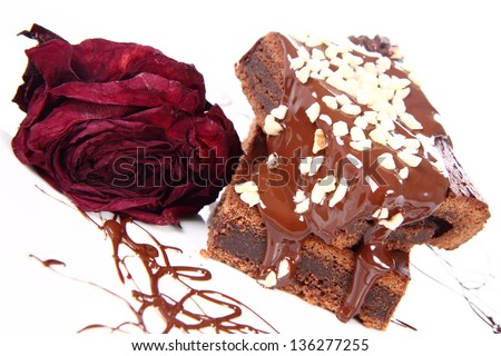 Slices of a brownie on a plate covered with chocolate and nuts, decorated with a dried rose flower