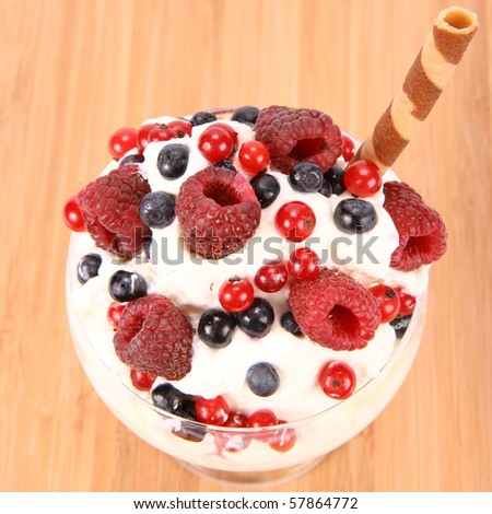 Whipped cream with raspberries, red currants and blue berries in a glass cup, decorated with a wafer tube on wooden background