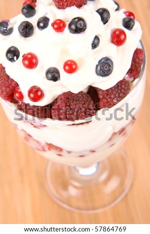 Whipped cream with raspberries, red currants and blue berries in a glass cup, decorated with a wafer tube on wooden background