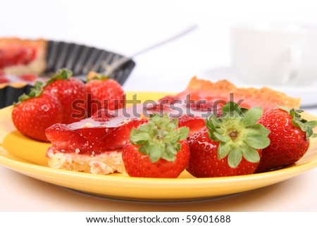 Piece of Strawberry Tart on a yellow plate decorated with strawberries with a cup of coffee and a tart pan in the background